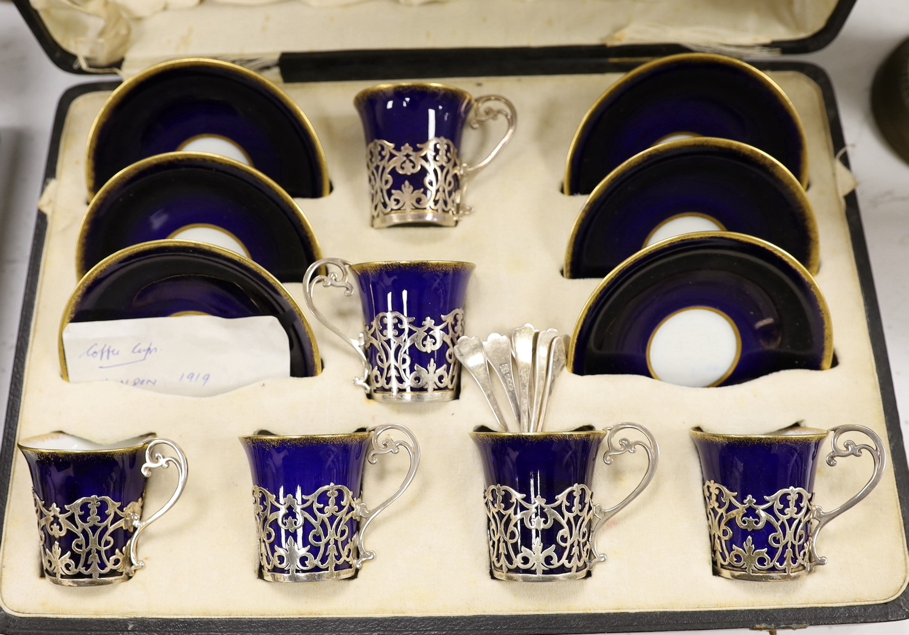 A set of six blue and gilt edged coffee cups and saucers, the cups with pierced silver holders, London, 1919, together with a set of 6 coffee spoons, triffid end terminals, Sheffield, 1925, cased